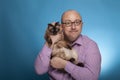 A businessman in a piked shirt holds a birman cat in the hand