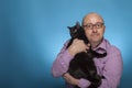 A businessman in a piked shirt holds a black cat in the hand