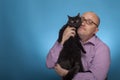 A businessman in a piked shirt holds a black cat in the hand