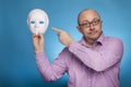 A businessman in a piked shirt holds a white mask, second face in his hand Royalty Free Stock Photo