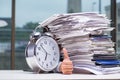 Businessman with pile stack of paper paperwork and an alarm cloc