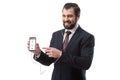 Cheerful bearded businessman listening music with earphones and pointing at smartphone with instagram website