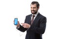 Cheerful bearded businessman listening music with earphones and pointing at smartphone with twitter website