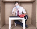 Businessman pointing to a protective mask, sitting in his little cardboard office