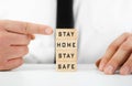 Man pointing to Stay Home, Stay Safe written on wooden blocks in a conceptual image for self quarantine times during virus
