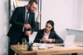 businessman pointing at watch near concentrated businesswoman at workplace with laptop Royalty Free Stock Photo