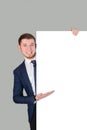 The businessman points with his palm at the white blank board, standing on a gray background Royalty Free Stock Photo