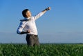 Businessman posing in a field, he goes in for sports and does strikes like martial arts or superman, green grass and blue sky as