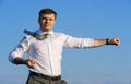 Businessman posing in a field, he goes in for sports and does strikes like martial arts or superman, green grass and blue sky as