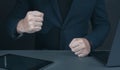 Businessman pounding fist on table, cropped image. Businessman with clenched fist on desk at dark office. Angry and furious