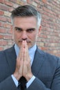 Businessman praying. Thoughtful mature man in formalwear holding hands clasped near face and while standing against brick wall Royalty Free Stock Photo