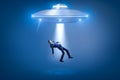 A businessman pulled toward an open hatch of a UFO by some invisible force.