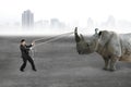 Businessman pulling rope against rhinoceros on concrete floor Royalty Free Stock Photo