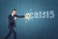 Businessman punching hard the word `crisis` written on dark blue wall.