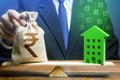 Businessman puts indian rupee money bag on scales and green house. Investment in renovation. Reduced CO2 emissions, energy Royalty Free Stock Photo