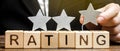 Businessman puts the third star above the word Rating on wooden blocks. The concept of quality of service. Hotel or restaurant