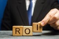 Businessman puts wooden blocks with the word ROI. Return on investment concept. Profitability and loss-making of investments. ROMI Royalty Free Stock Photo