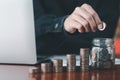 Businessman putting a coin on a glass piggy bank with stack coins, laptop. Saving money, bank deposits, interest collection and Royalty Free Stock Photo