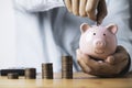 Businessman putting coin to pink piggy bank with increasing coins stacking on table , Money saving and deposit for investment to