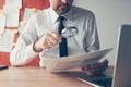 Businessman reading document contract papers with magnifying glass at office desk