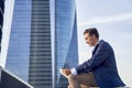 Businessman reading email received on a modern tablet while sitting outdoors in front of an office building, Caucasian Royalty Free Stock Photo