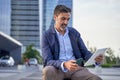 Businessman reading email received on a modern tablet while sitting outdoors in front of an office building, Caucasian Royalty Free Stock Photo