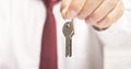 Businessman realtor offering keys to camera sitting at office table in shirt and red tie