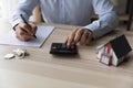 Businessman realtor using calculator, sitting at desk with house mockup