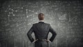 Businessman rear view with hands on hips thinking in front of a blackboard background written with different formulas and Royalty Free Stock Photo
