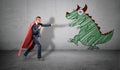 A businessman in a red cape standing in fighting pose ready to fight a picture of a dragon on the nearest wall. Royalty Free Stock Photo