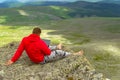 businessman in a red sweatshirt is sitting on a rock on a mountainside barefoot in seclusion with a noteboock in hand against a b Royalty Free Stock Photo