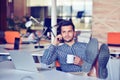 Businessman relaxing with legs up on desk, drinking coffee while dreaming about future at workplace in modern office. Royalty Free Stock Photo