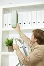 Businessman removing green folder from shelf