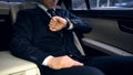 Businessman riding on backseat in luxury car, looking at watch, late for meeting