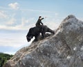 Businessman riding black bear climbing on mountain peak with sky