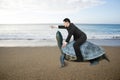 Businessman riding turtle and indicating with finger at sand bea