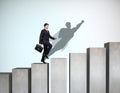 Businessman rise up on the career ladder with superhero shadow on the wall. Royalty Free Stock Photo