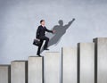 Businessman rise up on the career ladder with superhero shadow on the wall. Royalty Free Stock Photo