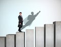 Businessman rise up on the career ladder with superhero shadow on the wall. Royalty Free Stock Photo
