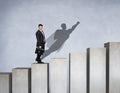 Businessman rise up on the career ladder with superhero shadow on the wall.