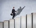 Businessman rise up on the career ladder with superhero shadow on the wall. Royalty Free Stock Photo