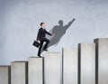 Businessman rise up on the career ladder with superhero shadow on the wall. Royalty Free Stock Photo