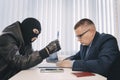 businessman and robbers are sitting at a table. A racketeer in a black balaclava forces to sign a contract. The concept Royalty Free Stock Photo