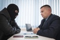 businessman and robbers are sitting at a table. A racketeer in a black balaclava forces to sign a contract. The concept