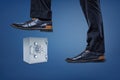Businessman`s feet in leather shoes ready to smash a light grey metal safe.