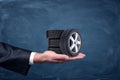 A businessman`s hand on blue chalkboard background holding four tiny car wheels. Royalty Free Stock Photo