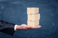 A businessman`s hand holding a set of small three cardboard boxes palm up on chalkboard background.