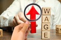 Businessman`s hand holds red arrow up near wooden blocks with word Wage. Salary increase concept. Wages rate. Revenue growth and