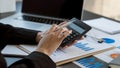 Businessman`s hands pressing a calculator, calculating, analyzing, graphing, charting, accounting worker working on a laptop. A ba