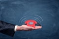 A businessman`s palm hold a small red retro dial phone with lines showing soundwave emissions. Royalty Free Stock Photo